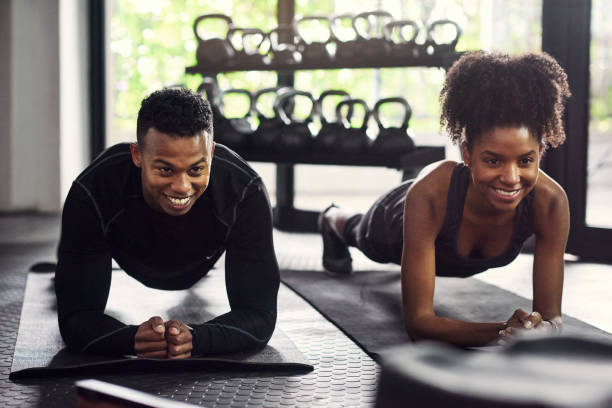 shot of a young man and woman doing plank exercises together in a gym